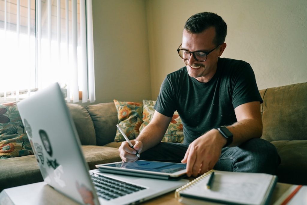 A coach in a black t-shirt working on a MacBook Air, messaging warm LinkedIn leads by hand from a home office.