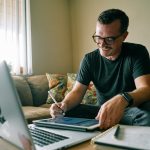 A coach in a black t-shirt working on a MacBook Air, messaging warm LinkedIn leads by hand from a home office.