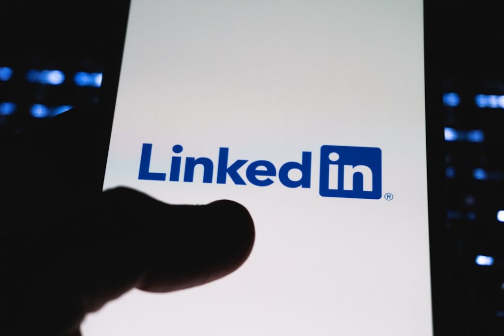 The LinkedIn app icon glowing on a smartphone screen held in one hand, representing day-to-day LinkedIn networking and engagement before outreach.