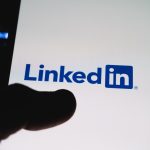 The LinkedIn app icon glowing on a smartphone screen held in one hand, representing day-to-day LinkedIn networking and engagement before outreach.
