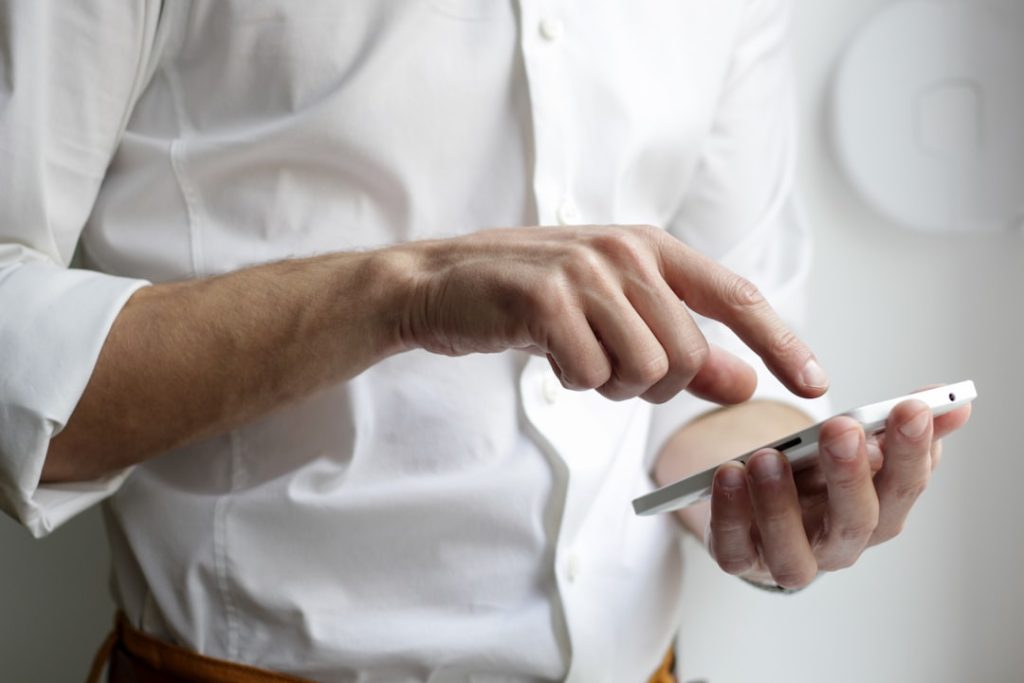 Close-up of a person in a white shirt tapping out a message on a smartphone, illustrating a personalized LinkedIn outreach message.