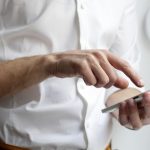 Close-up of a person in a white shirt tapping out a message on a smartphone, illustrating a personalized LinkedIn outreach message.