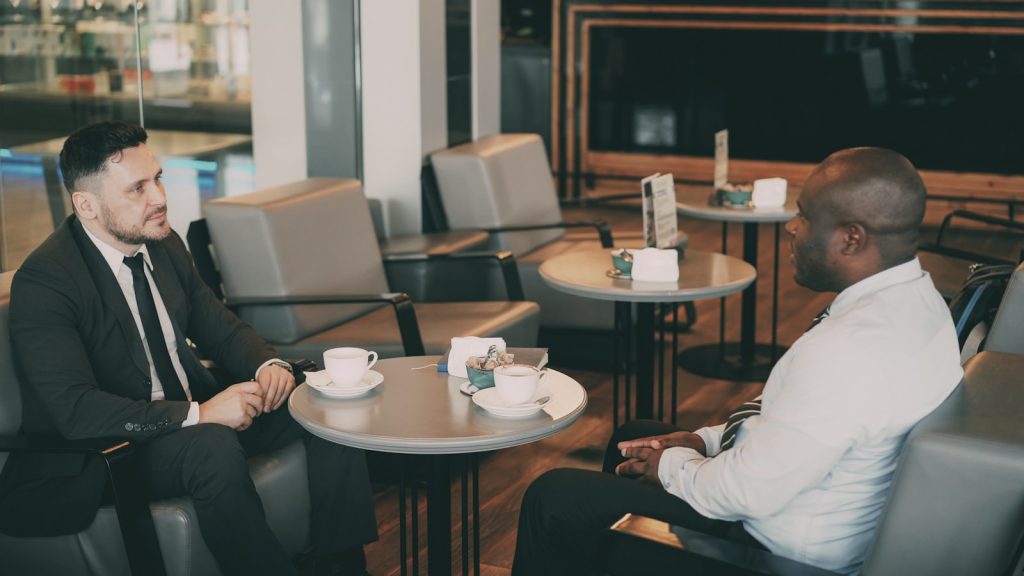 Two professionals having a warm one-on-one conversation at a cafe, illustrating a warm-first LinkedIn outreach strategy