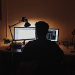 A lone founder working late at a dual-monitor desk in a dimly lit room, running outbound sales solo instead of hiring an SDR team.