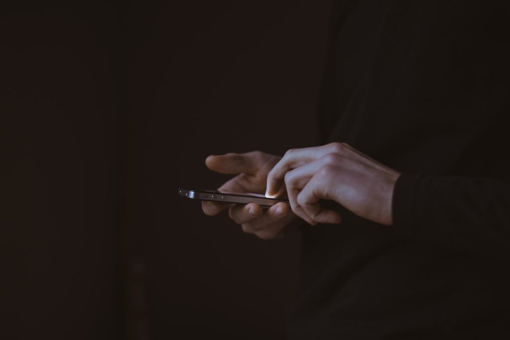 A person silhouetted against bright daylight, holding a smartphone and composing a short message.