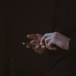 A person silhouetted against bright daylight, holding a smartphone and composing a short message.