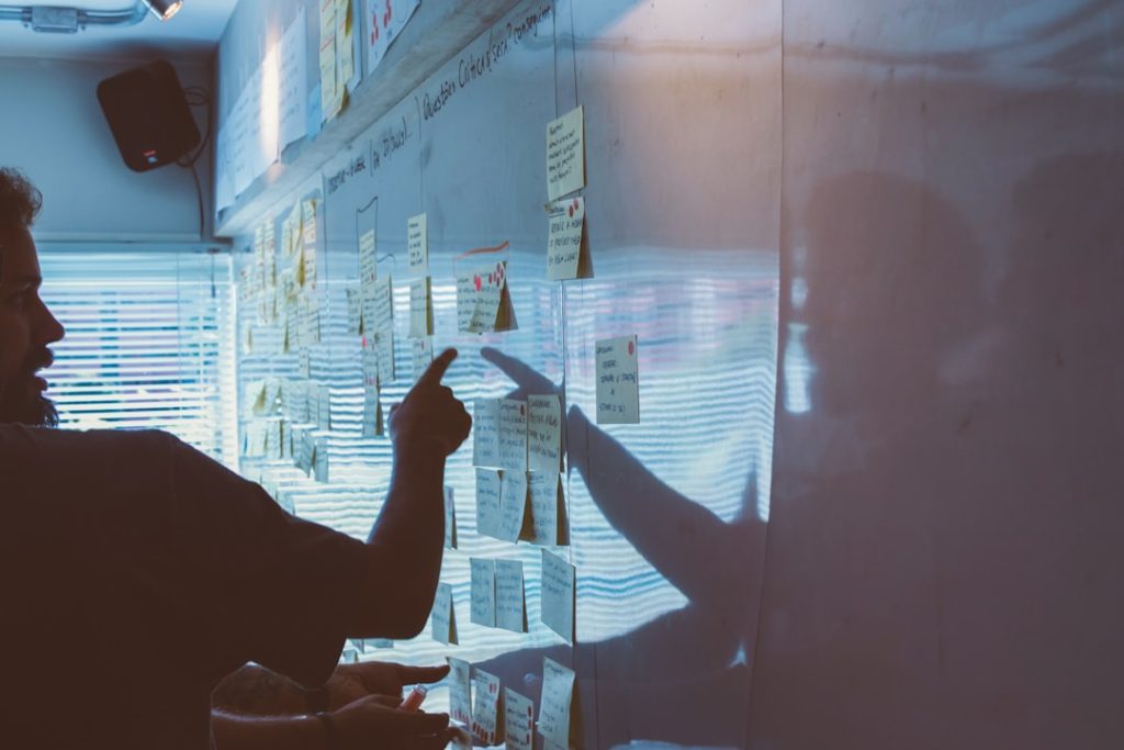 A person points at a wall covered in handwritten sticky notes and index cards while mapping out a marketing strategy