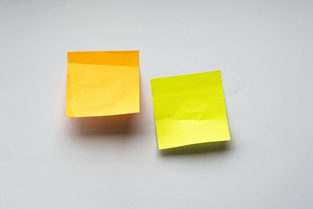 Two blank sticky notes, one orange and one yellow, stuck side by side on a plain white wall.
