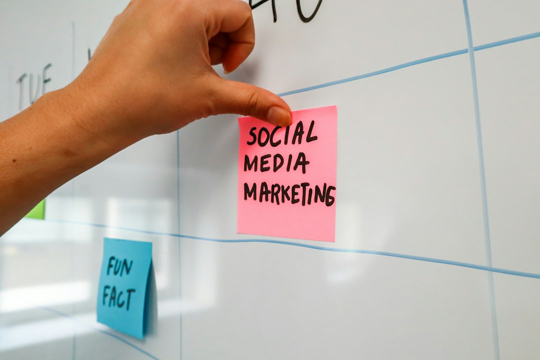 A hand pressing a pink sticky note reading "Social Media Marketing" onto a whiteboard planning grid, with a blue "Fun Fact" note below it.
