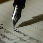 Close-up of a fountain pen nib writing cursive handwriting on lined paper, with the pen's shadow falling across the page.