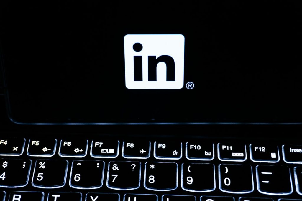 The white LinkedIn logo on a black laptop screen above a backlit keyboard in a dark room.