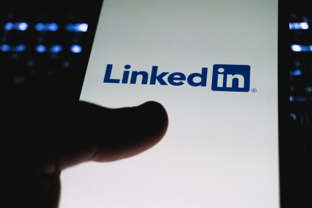 A dark silhouette of a thumb hovering over a phone screen that shows the LinkedIn logo on a white background.
